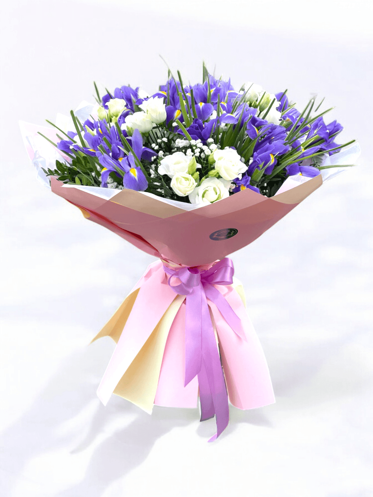 Buchet flori irisi eustoma cu 23 irisi mov și 6 eustoma albe, decorat cu verdeață și ambalaj elegant roz. Ideal pentru cadouri și ocazii speciale.
