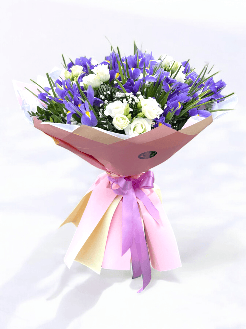 Buchet flori irisi eustoma cu 23 irisi mov și 6 eustoma albe, decorat cu verdeață și ambalaj elegant roz. Ideal pentru cadouri și ocazii speciale.